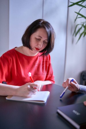 woman is writing down important points at a meeting in the office                    