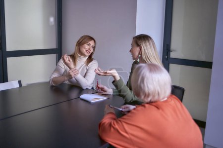  women, including a person with a disability, discuss the company's strategy at a meeting in the office                       