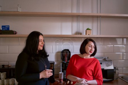     two women talking over coffee in the office kitchen                               