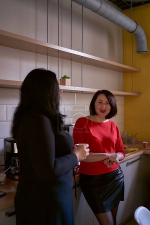     two women talking over coffee in the office kitchen                               