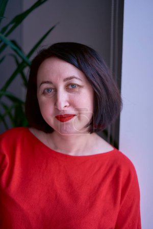 a portrait of a brunette with a bob haircut in a red sweater and a leather mini skirt in the office                    