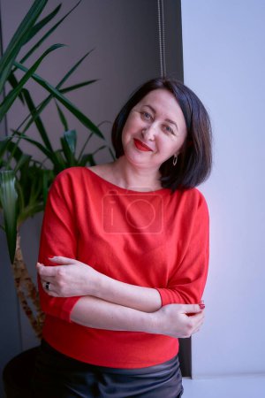 a portrait of a brunette with a bob haircut in a red sweater and a leather mini skirt in the office                    