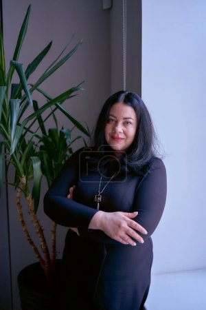                  Porträt einer mittelgroßen Frau mit schwarzen Haaren in einem schwarzen Kleid in einem Büro              