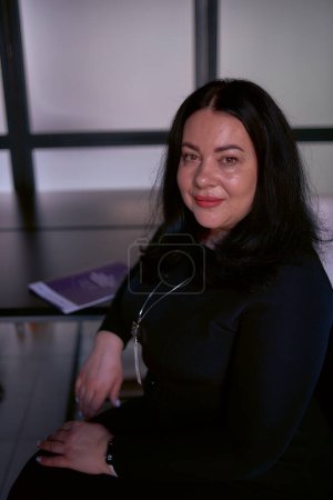                  Porträt einer mittelgroßen Frau mit schwarzen Haaren in einem schwarzen Kleid in einem Büro              