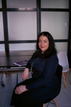                  portrait of a medium size woman with black hair in a black dress in an office              