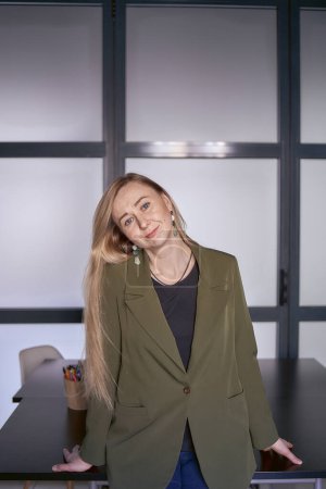Téléchargez les photos : Femme blonde aux cheveux longs dans une veste verte et un jean dans le bureau - en image libre de droit