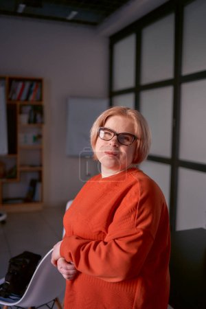 portrait of a woman with a disability in an orange sweater and leather pants in the office               