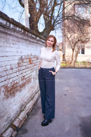         a beautiful middle age woman in a sweater and  chic wide leg pants  outside on a spring day                       