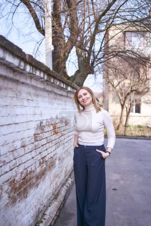         a beautiful middle age woman in a sweater and  chic wide leg pants  outside on a spring day                       