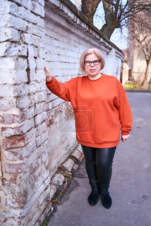               portrait of a disabled woman in an orange sweater and leather pants on a spring day                 