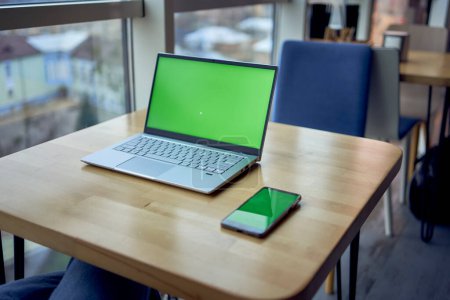       a laptop and phone with green screen on single workplace table, chroma key,                         