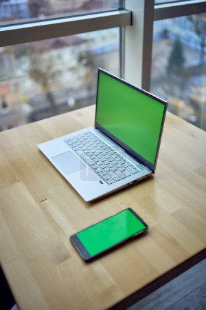       a laptop and phone with green screen on single workplace table, chroma key,                      