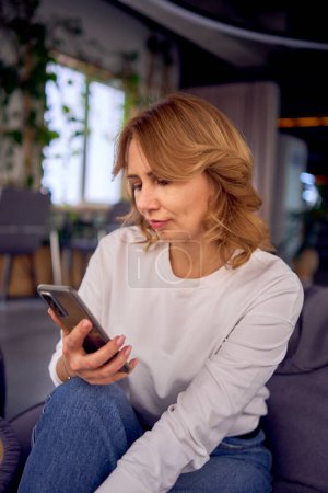  Frau in Freizeitkleidung sitzt auf einem Bohnensack und sucht mit dem Handy                   