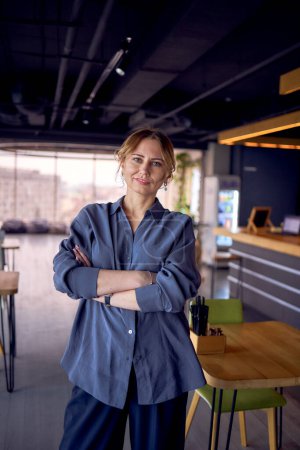           attractive middle age woman with crossed arms in a modern coworking neutral design, wearing wide leg pants and a silk blouse                                                 