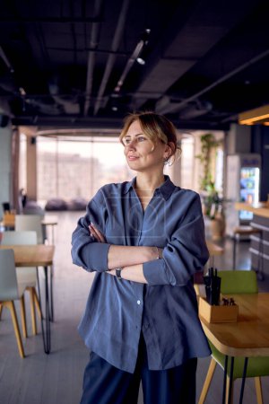           attractive middle age woman with crossed arms in a modern coworking neutral design, wearing wide leg pants and a silk blouse                                                 