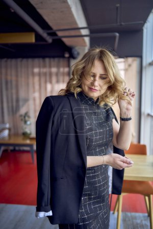 Téléchargez les photos : Une femme séduisante dans une mini-robe et une veste de style business noir laisse tomber ses cheveux dans un espace de coworking de style loft moderne - en image libre de droit