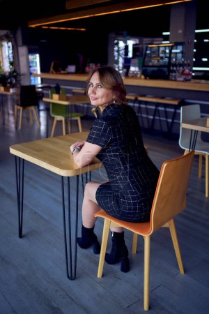 eine atemberaubende junge erwachsene Frau in einer modernen Café-Bar sitzt an einem Tisch                  