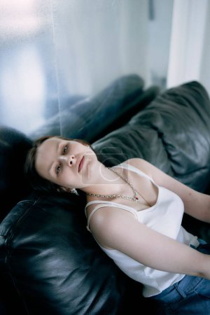 a young teenage girl fighting brain cancer at photo shoot in studio, metal wall, reflection, black sofa