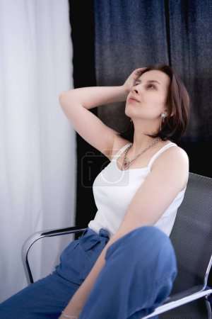 una joven adolescente luchando contra el cáncer de cerebro en sesión de fotos en el estudio sentado en la silla entre cortinas blancas
