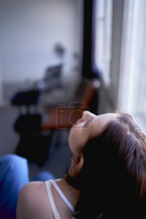 a young teenage girl fighting brain cancer in a studio photo shoot sitting on a chair by the window                      