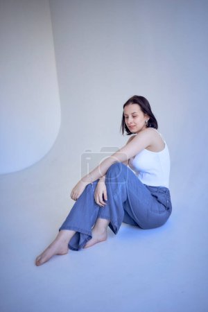 a young teenage girl sits on a white cyclorama in the studio                      