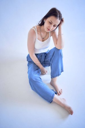 una joven adolescente se sienta en un cyclorama blanco en el estudio                      