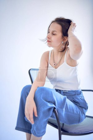 ein junges Teenager-Mädchen, das gegen Gehirnkrebs kämpft, sitzt auf einem schwarzen Stuhl vor weißem Hintergrund im Studio         