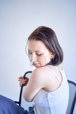 ein junges Teenager-Mädchen, das gegen Gehirnkrebs kämpft, sitzt auf einem schwarzen Stuhl vor weißem Hintergrund im Studio         