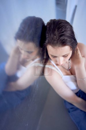 a young teenage girl fighting brain cancer at photo shoot in studio sitting on floor, leaning against metal wall, reflection