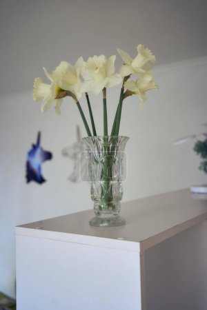 a  daffodils in a crystal vase on a shelf                       