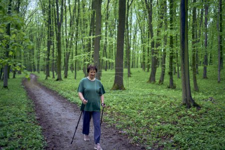 una anciana se dedica a caminar nórdico con palos en el bosque de primavera