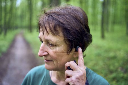  una anciana que se dedica a caminar nórdico con palos en el bosque de primavera cambia la música en los auriculares                        