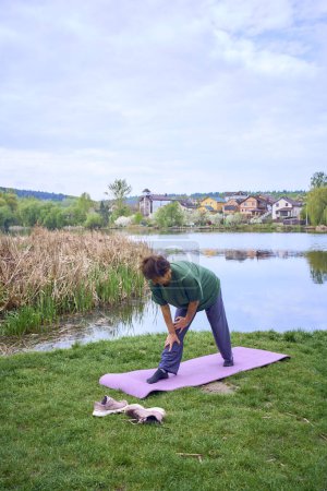 Téléchargez les photos : Une vieille femme faisant des exercices le matin sur la rive de la rivière, un vélo et un yogamat à côté d'elle - en image libre de droit