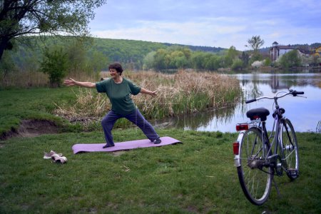 an old woman practices yoga in the morning on the river bank, came from home by bicycle