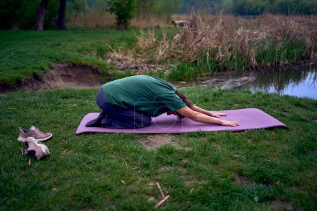 an old woman practices yoga in the morning on the river bank, came from home by bicycle