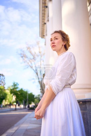 an elegant middle age woman in white vintage dress near theater with antique colonnades