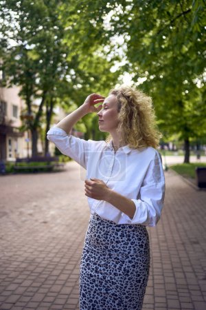 Photo for Beautiful middle age woman in 70s, 80s style clothes stretches after work on a sun drenched alley - Royalty Free Image