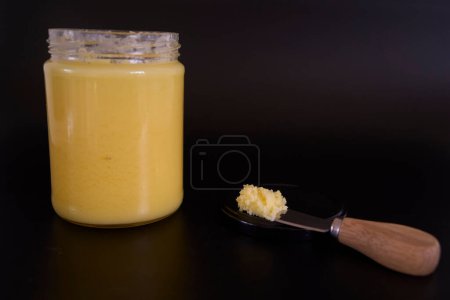 Butter-Ghee in einem transparenten Glas mit hausgemachtem Brot auf schwarzem Hintergrund