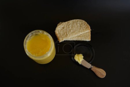 ghee au beurre dans un bocal transparent avec du pain fait maison sur fond noir