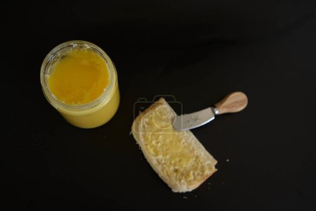 Butter-Ghee in einem transparenten Glas mit hausgemachtem Brot auf schwarzem Hintergrund