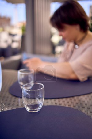 une femme taille plus en robe fuzz pêche choisit un plat dans un restaurant via QR code dans smartphone, de l'eau avec du citron et des lunettes devant elle                   