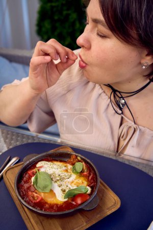 une femme de taille moyenne en robe fuzz pêche manger Shakshouka dans un restaurant moderne