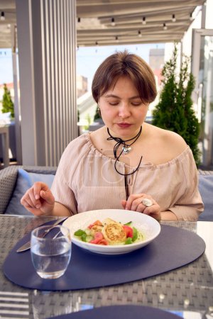 una mujer de tamaño mediano en vestido de pelusa de melocotón comer tortitas de queso cottage con salmón y espinacas en el restaurante moderno                            