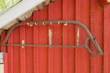 Old rusty bow saw (swede saw, finn saw or bucksaw) hanging on wooden wall of traditionally red painted building.