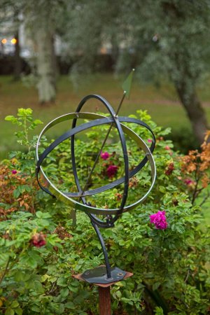 Metal sun clock in a garden surrounded by plants.