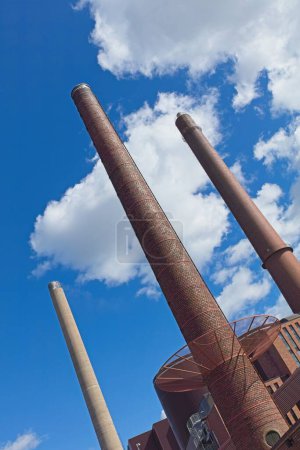 Old tall red brick chimneys against blue sky with white clouds in summer.