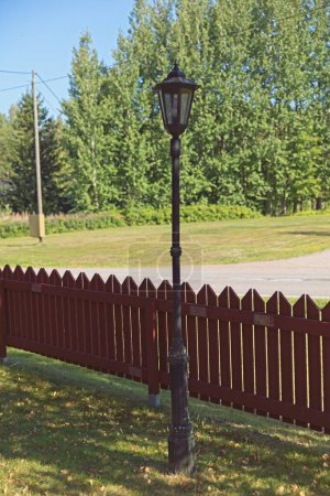Old style metal street lamp and red wooden picket fence in summer.