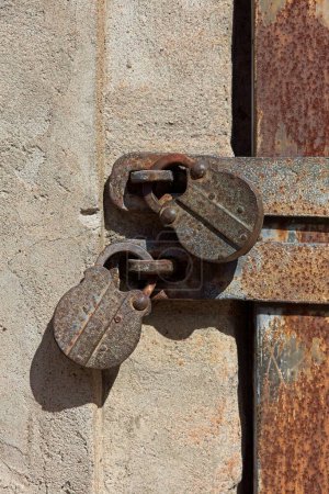 Closeup of two old rusty padlocks on a stone building with metal door barred.