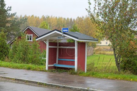 Red wood bus stop shelter in countryside in cloudy autumn weather.