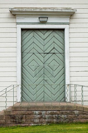 Puertas dobles pintadas de color verde claro en un edificio de madera blanca con escalones de roca.